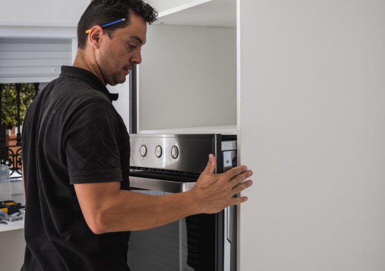 Caucasian adult male placing an oven inside the hole of a kitchen cabinet he is assembling for a customer.